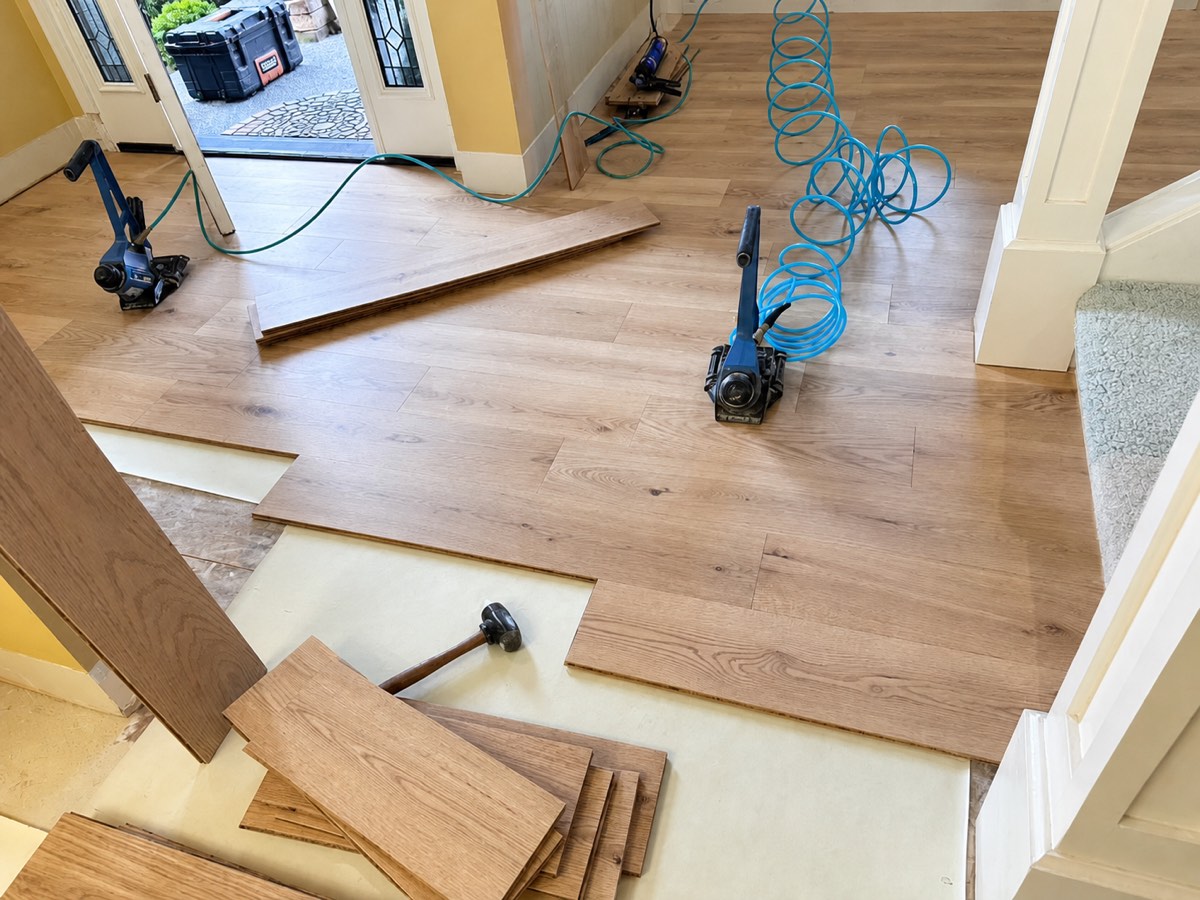 Oak herringbone hardwood being installed in an entryway with flooring nailers